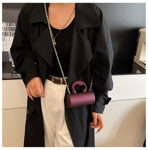Détail d'un sac cylindrique violet avec bandoulière dorée porté par un mannequin