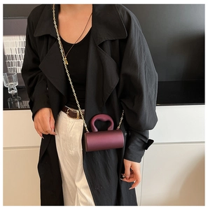 Detail of burgundy cylindrical mini bag with golden chain and sleek U-shaped handle