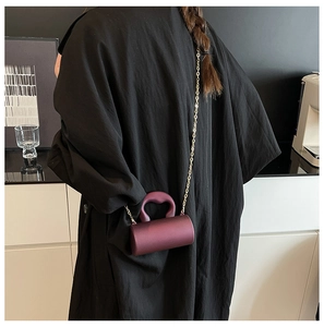 Chic burgundy acrylic cylinder bag with gold chain strap shown on a black coat outfit