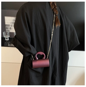 Detail of dark purple cylindrical acrylic evening bag with gold chain and handle