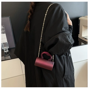 Gros plan d'un sac cylindrique en satin violet avec chaîne dorée porté par un mannequin