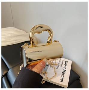 Detail of a golden cylindrical handbag with a glossy metallic finish and chunky top handle