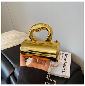 Macro detail of glossy gold cylindrical handbag with thick handle and metallic chain strap