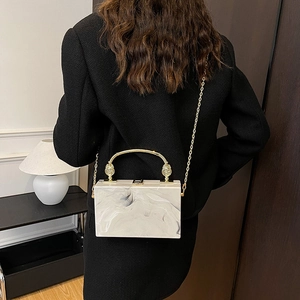 Elegant white marble acrylic clutch bag with gold handle shown on a black suit blazer