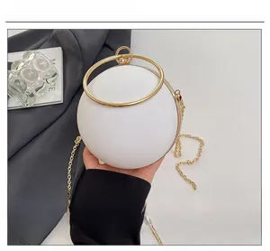 Macro shot of white spherical evening bag with golden ring handle and chain strap
