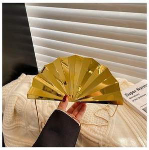 Detail of a golden fan-shaped acrylic evening clutch with mirror finish and metal chain