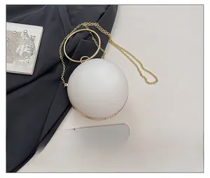 Detailed view of round white acrylic clutch bag with gold handle and metal chain strap