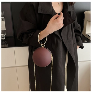 Close-up of a burgundy round evening bag with gold ring handle and metal chain strap