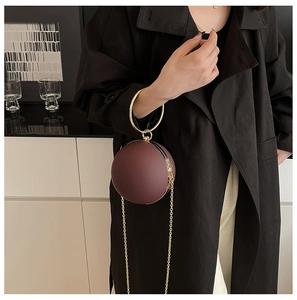 Detail of wine red spherical clutch with gold ring handle on a black coat outfit