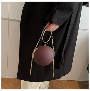 Detail of round burgundy evening clutch featuring a gold circular handle and metal chain strap