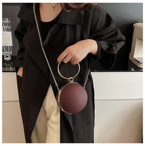 Detail of burgundy spherical clutch with gold circular handle and crossbody chain strap