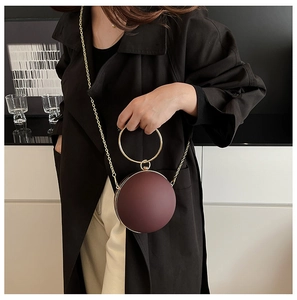 Detail of burgundy sphere bag with gold circular handle and matte leather texture