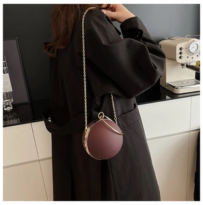 Detailed view of dark plum acrylic spherical clutch with golden hardware and chain strap