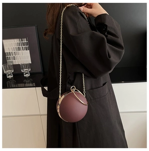 Detail of spherical evening bag in deep purple with golden ring handle and chain strap
