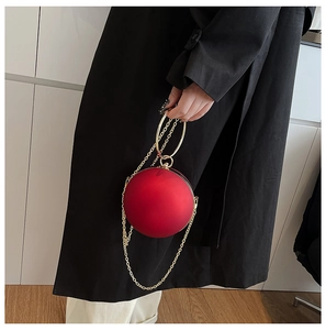 Detail of red spherical evening bag with golden ring handle and chain strap on model
