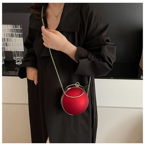 Chic red sphere evening bag with gold ring handle worn over a black trench coat