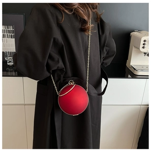 Detail of red spherical evening clutch bag with gold handle on black coat background