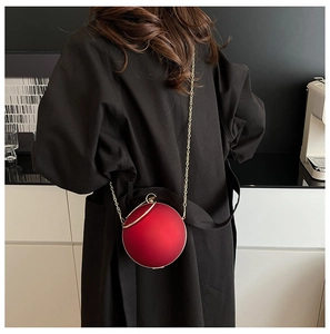 Red acrylic ball handbag with gold chain on black trench coat for evening fashion style