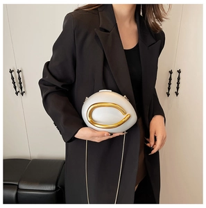 Detail of white oval hard shell evening clutch with gold circular metal accent and chain