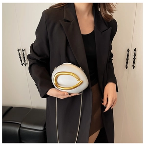 Detail of a metallic clutch with gold C-shaped ring handle and a slim chain strap