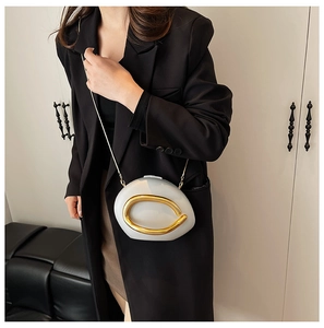 Detail of white oval crossbody bag with gold horseshoe clasp and metal chain on model
