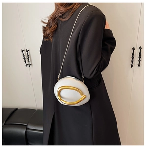 Detail of white egg-shaped acrylic clutch with gold C-shaped metal hardware on black suit