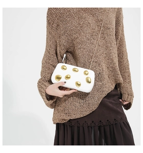 Close-up of white hard-shell crossbody bag with artistic gold pebble-shaped metal accents