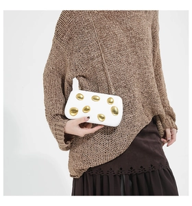 Detail of elegant white clutch bag with gold pebble accents and a gold chain strap