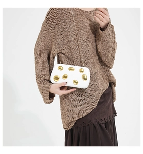 Elegant white clutch bag with gold pebble studs worn by a model in a knit outfit