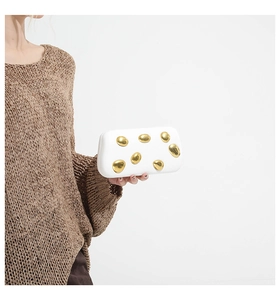 Detailed close-up of white evening clutch bag featuring artistic golden stone embellishments