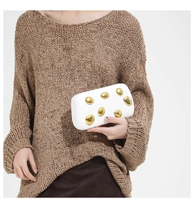 Macro shot of a white rectangular clutch bag featuring an artistic gold pebble metal buckle