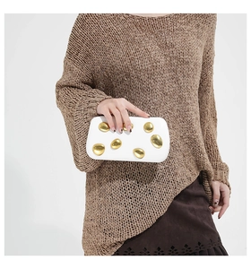 Macro shot of white rectangle clutch bag featuring artistic gold pebble-shaped buckles