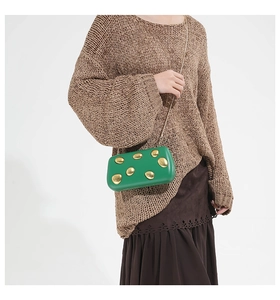 Detail of green metallic clutch bag with golden circular studs and metal chain strap