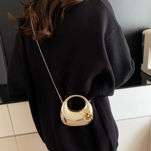 Golden crescent handbag with a metal flower and chain strap shown on a black sweater