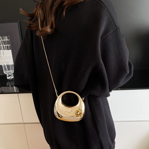 Detail of a gold metallic half-moon clutch bag featuring floral gemstone and chain strap