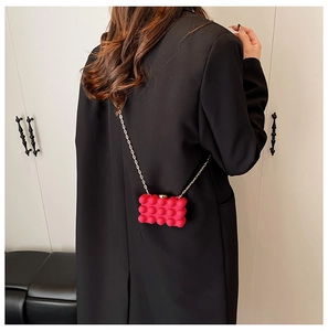 Detail of red bubble-textured acrylic mini bag with gold chain on black blazer