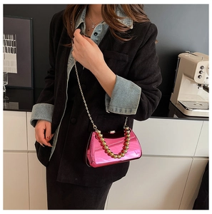 Close-up of bright pink acrylic evening bag with golden chain and beaded handle on a model