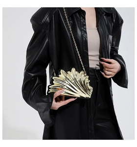 Detail of a gold metallic shell evening clutch bag with fine chain on leather jacket
