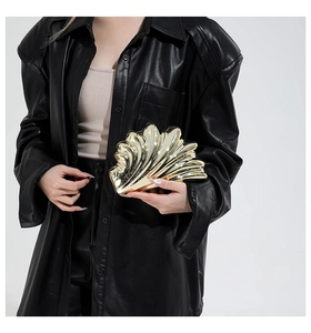 Detail shot of a golden shell-shaped clutch bag with polished metallic stripe texture