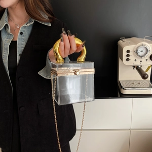 Detail view of transparent acrylic cylinder box bag with bold golden horseshoe handle