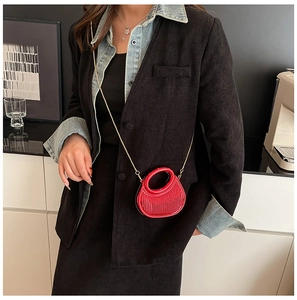 Model wearing a red acrylic pleated half-moon mini bag with a delicate gold chain strap