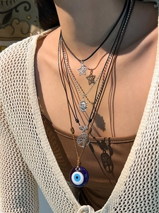 Detail of layered bohemian necklace featuring evil eye, sun, and tree of life charms