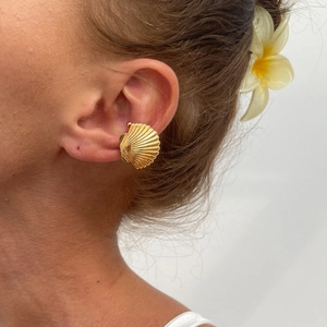 Golden seashell ear cuff with radial texture, worn for a stylish summer beach vacation look