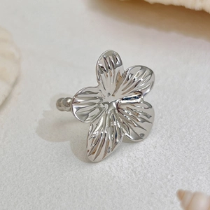 Macro shot of silver five-petal flower ring with grooved texture on shell background