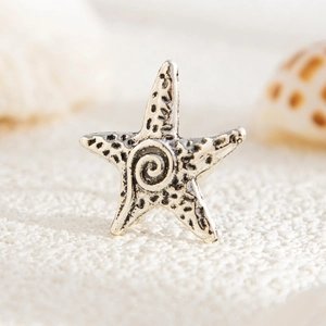 Macro shot of silver starfish ear cuff with vintage black spots on white sand