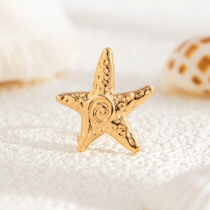 Golden starfish earring with textured surface and spiral center on white sand background