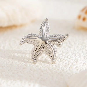 Macro view of silver starfish ear cuff with beaded texture on a white beach background