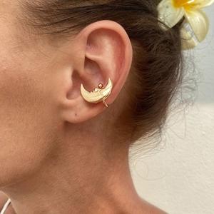Detailed close-up of a gold crescent ear cuff with carved face detail on female model