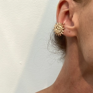 Close-up of golden sun-shaped non-pierced ear cuff worn on the upper ear cartilage