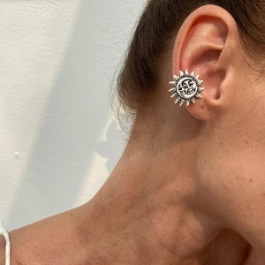 Macro shot of retro silver sun cartilage ear cuff featuring a radiant sunray relief design